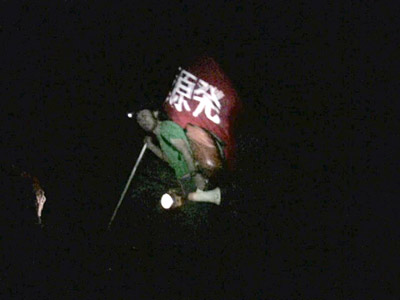Two large scale video projections, a guy is walking toward to the peak of Mt. Fuji on the left side, and a view of protest demonstration on the right side.