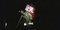 Two large scale video projections, a guy is walking toward to the peak of Mt. Fuji on the left side, and a view of protest demonstration on the right side.